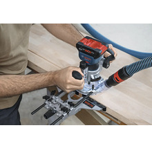 O freză superioară este utilizată pentru prelucrarea unei bucăți de lemn. Un furtun de aspirator este atașat la mașină.