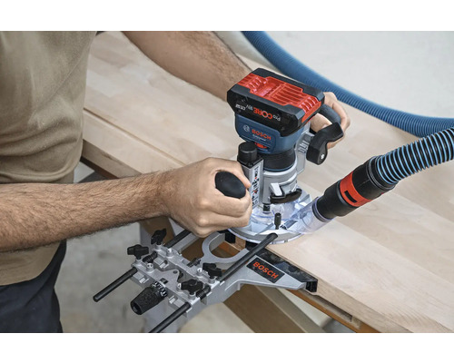 O freză superioară este utilizată pentru prelucrarea unei bucăți de lemn. Un furtun de aspirator este atașat la mașină.