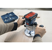 O persoană folosește o freză verticală Bosch pe o scândură de lemn. Un set de freze se află în apropiere.