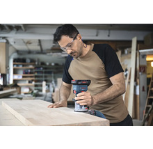 Un bărbat folosește o freză verticală Bosch pe o scândură de lemn într-un atelier.