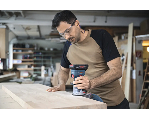 Un bărbat folosește o freză verticală Bosch pe o scândură de lemn într-un atelier.