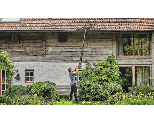 Un bărbat curăță jgheabul cu un curățător de jgheaburi în fața unei case.