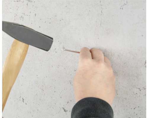 O persoană bate un cui în perete cu un ciocan.