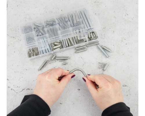 Asortiment de arcuri de tracțiune diferite într-o cutie transparentă din plastic, un arc este ținut de două mâini