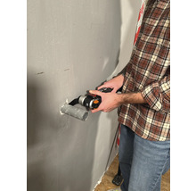 Un bărbat taie o țeavă cu o unealtă multifuncțională pe un perete.