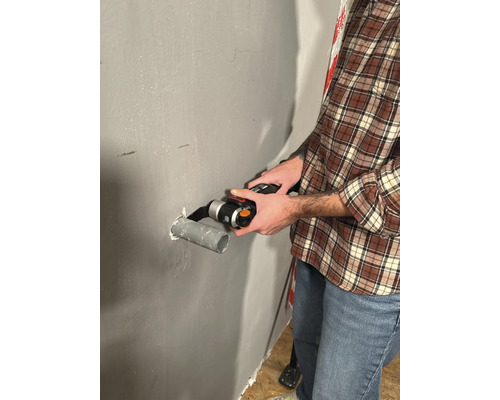 Un bărbat taie o țeavă cu o unealtă multifuncțională pe un perete.