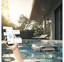 Persoană care controlează un robot de curățare a piscinei cu un smartphone într-o piscină exterioară