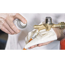 O persoană curăță un regulator de presiune a gazului cu un spray și o cârpă.