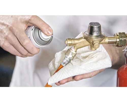 O persoană curăță un regulator de presiune a gazului cu un spray și o cârpă.