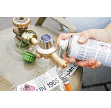 Persoană pulverizând detergent pe racordul buteliei de gaz