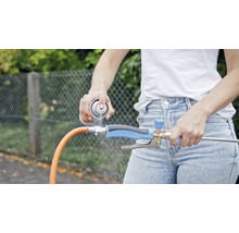 O persoană pulverizează detergent pe un regulator de jet de apă conectat la un furtun de grădină.