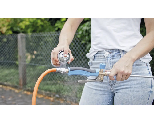 O persoană pulverizează detergent pe un regulator de jet de apă conectat la un furtun de grădină.