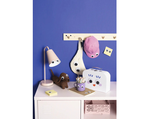 Mobilier decorativ pentru copii cu lampă, taburet, cuier, geantă, șapcă, blocnotes, cutie de prânz și creioane pe o comodă în fața unui perete albastru