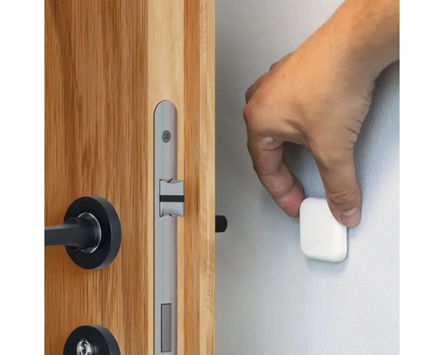 O mână atașează un opritor magnetic de ușă pe un perete lângă o ușă de lemn cu o broască argintie.