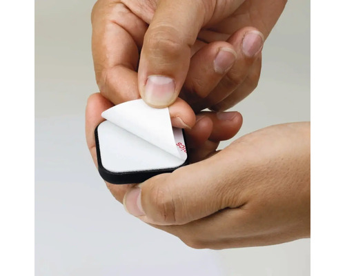 O mână îndepărtează folia de protecție de pe un glisor autoadeziv pentru mobilă.