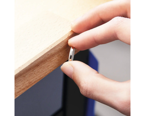 O persoană ține o bucată subțire, rotundă, de metal de o margine de lemn.