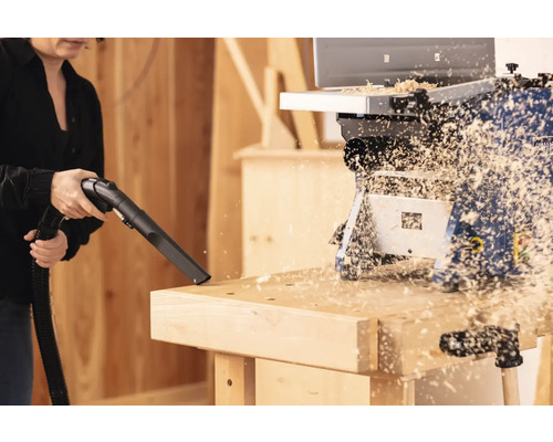 Femeie aspirând așchii de lemn de pe un banc de lucru cu un aspirator