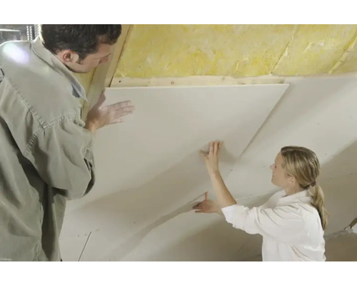 Două persoane fixează o placă de gips-carton pe un tavan