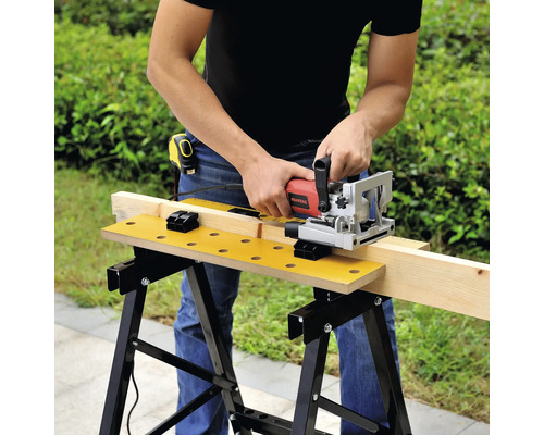 Un bărbat folosește o freză de îmbinări pe un banc de lucru pentru a prelucra o scândură de lemn.