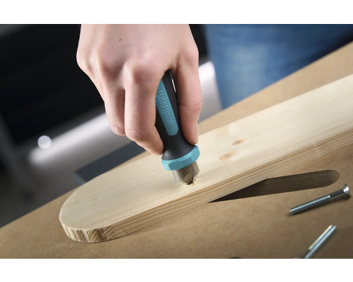 O mână coboară un burghiu de frezat marca Wolfcraft într-o scândură de lemn pentru a îngropa un șurub.