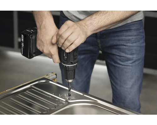 Un meșter găurește o chiuvetă cu o bormașină