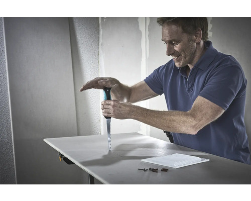 Un bărbat taie o placă de gips-carton cu un ferăstrău pe un banc de lucru.