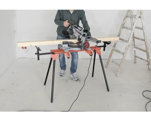 O persoană operează un ferăstrău circular pe o masă de tăiat, lângă o scară.