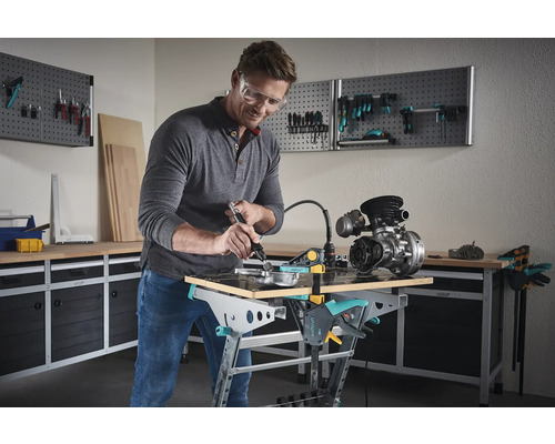 Un bărbat lucrează cu o unealtă multifuncțională pe o piesă de lucru pe un banc de lucru Wolfcraft într-un atelier.