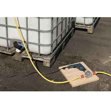 Scenă cu containere IBC, o mașină de găurit și o pompă de furtun pe o scândură.