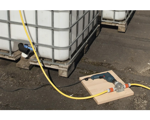 Scenă cu containere IBC, o mașină de găurit și o pompă de furtun pe o scândură.