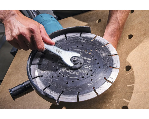 O persoană schimbă discul de tăiere cu o cheie pe un polizor unghiular