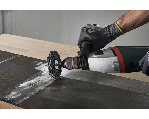 O perie de sârmă este utilizată cu o mașină de găurit pe o scândură de lemn.