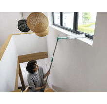 Femeie curăță rama ferestrei cu un pămătuf pe un suport telescopic în casa scării