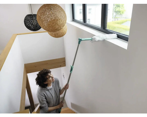 Femeie curăță rama ferestrei cu un pămătuf pe un suport telescopic în casa scării