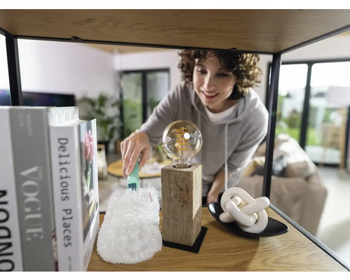 Femeie ștergând praful de pe un bec de pe un raft