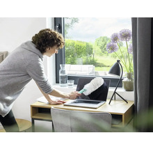 Femeie curăță laptopul cu un pămătuf pe birou.