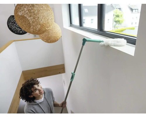 Femeie curăță pervazul ferestrei cu un pămătuf.