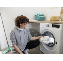 Femeie umple mașina de spălat cu cârpe de curățat, în timp ce un mop stă alături