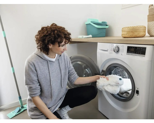 Femeie pune huse de mop în mașina de spălat într-o cameră luminoasă.