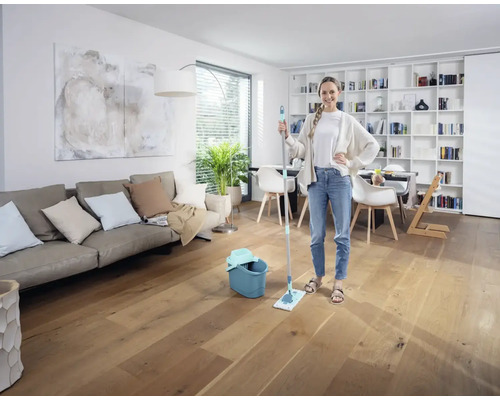 Femeie cu mop și găleată într-un living luminos pe o podea de lemn