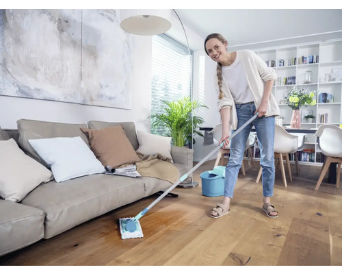 Femeie șterge parchetul din lemn în sufragerie cu mopul și găleata.
