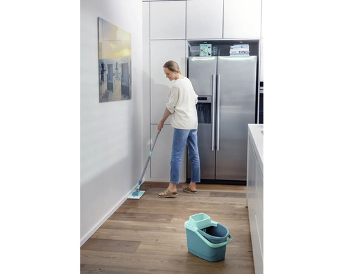 Femeie șterge podeaua cu un mop într-o bucătărie.