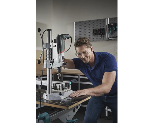 Bărbat cu ochelari de protecție găurind cu o mașină de găurit cu coloană într-un atelier