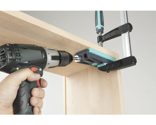 Mașină de înșurubat cu acumulator care găurește o scândură de lemn printr-un ghidaj de găurire