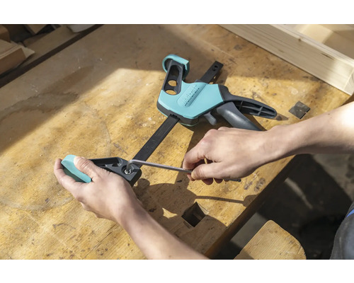 O persoană ajustează o menghină cu o singură mână cu o cheie imbus pe un banc de lucru.