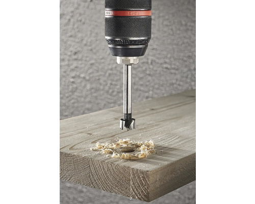 Burghiu Forstner care face o gaură într-o scândură de lemn, creând așchii de lemn.