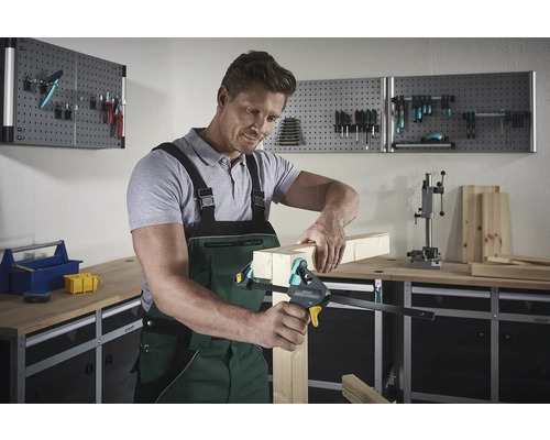 Bărbat fixează bucăți de lemn cu o menghină de o mână într-un atelier.