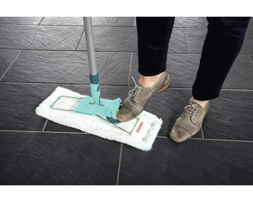 Mop utilizat pe gresie închisă la culoare, acționat de o persoană încălțată.