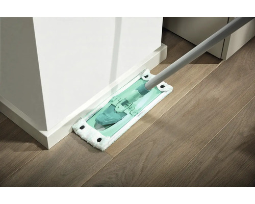 Mop cu husă din microfibre curăță o podea din lemn de lângă un perete alb.