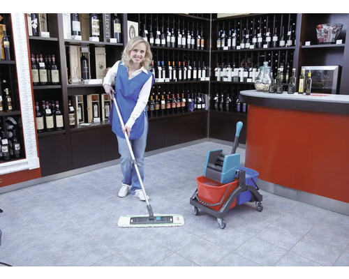 Femeie de serviciu șterge o podea de gresie într-un magazin de vinuri cu un mop și o găleată.